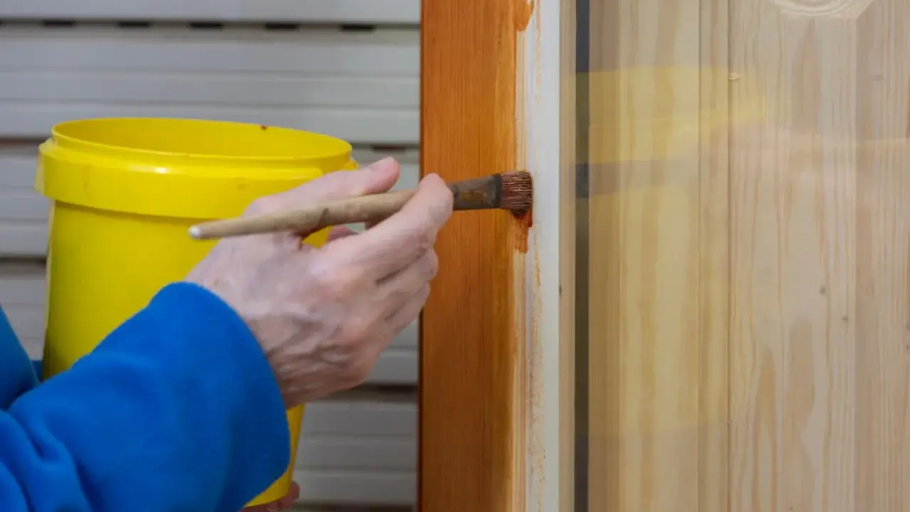 Persona aplica barniz a puerta de madera con brocha. Aprende como pintar puertas de madera para un acabado perfecto.