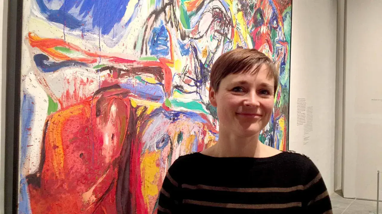 Kvinna ler framför en färgstark målning i Asger Jorns stil.