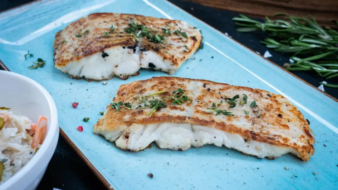 Zwei perfekt gegrillte Kabeljaufilets, mit Kräutern bestreut, serviert auf einem blauen Teller. Genießen Sie kabeljau grillen ohne alufolie!