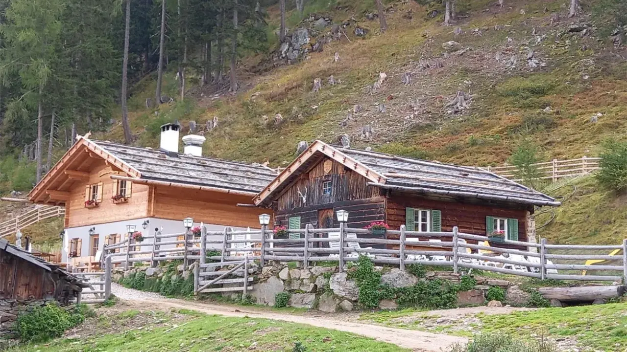 Tablander Alm a Parcines, con due baite in legno e recinzione, immerse nel verde di un pendio boscoso.