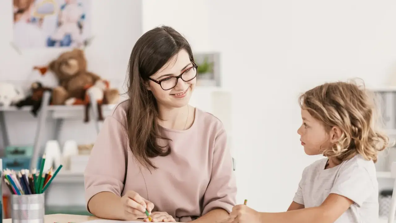 Bambina con ADHD, durante una sessione di diagnosi, disegna con una maestra sorridente.