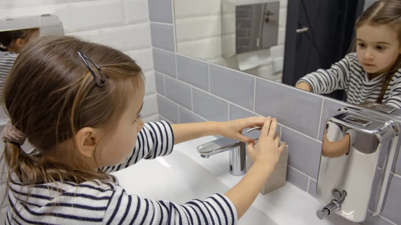 Niña se lava las manos en el baño, un gesto importante para la higiene y la prevención del toc en niños.