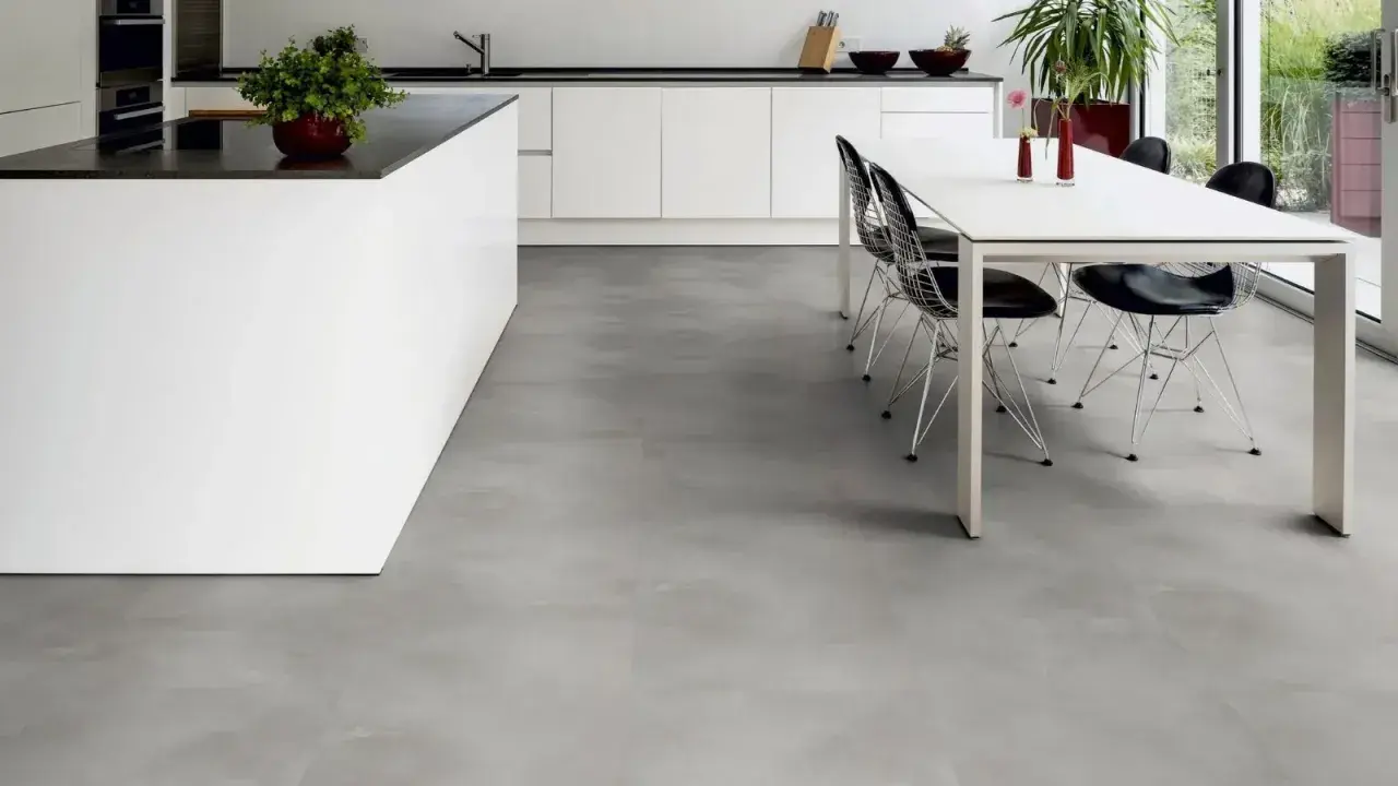 Cucina moderna con isola bianca e tavolo da pranzo. Il pavimento in LVT grigio effetto cemento completa l'ambiente minimalista.