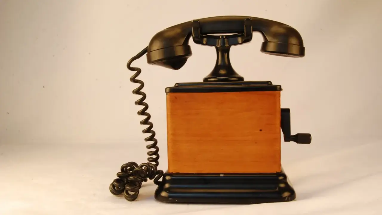 Stary telefon na korbkę z drewnianą obudową i czarną słuchawką.