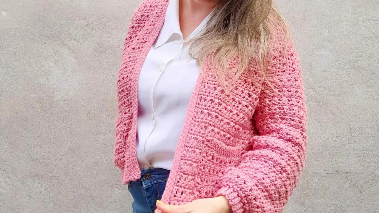 Mujer con un cardigan a crochet rosa, sobre una camisa blanca y jeans.