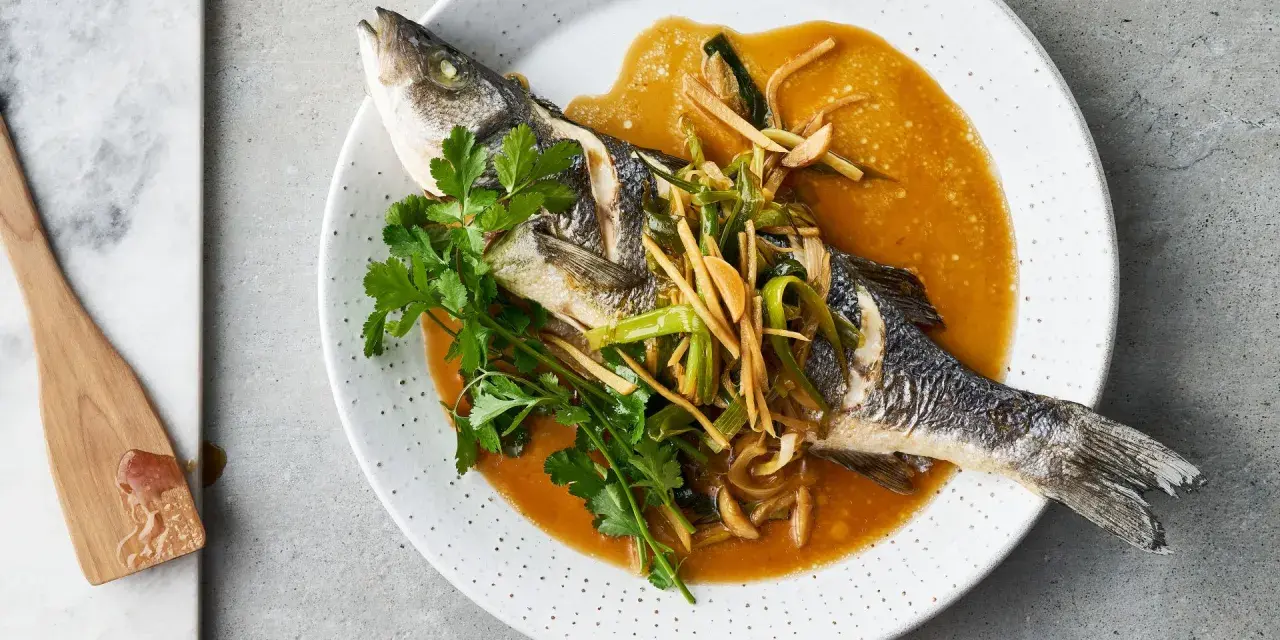 Ein ganzer Wolfsbarsch Fisch, gedünstet in einer würzigen Sauce mit Ingwer und Frühlingszwiebeln, garniert mit Koriander.