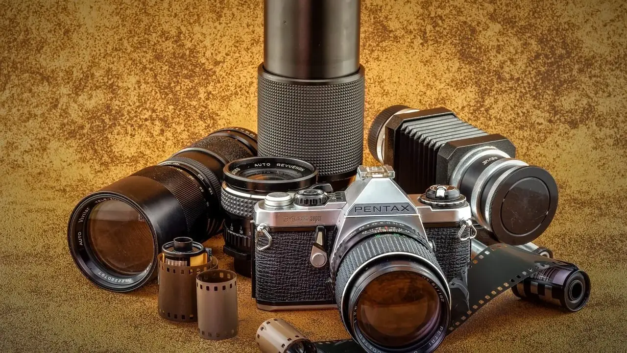 Kolekcja sprzętu fotograficznego: aparat Pentax JMC Super, obiektywy, mieszek i klisze.