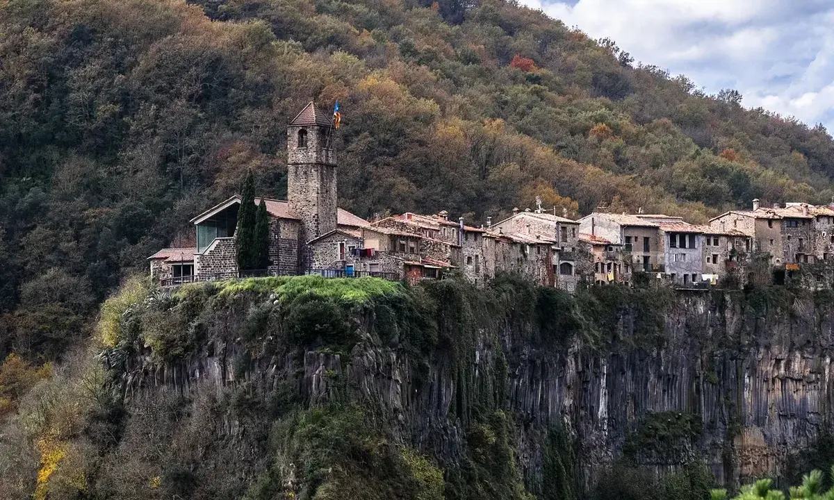 Castellfollit de la Roca, un pueblo medieval colgado sobre un acantilado basáltico, se alza majestuoso entre bosques otoñales.