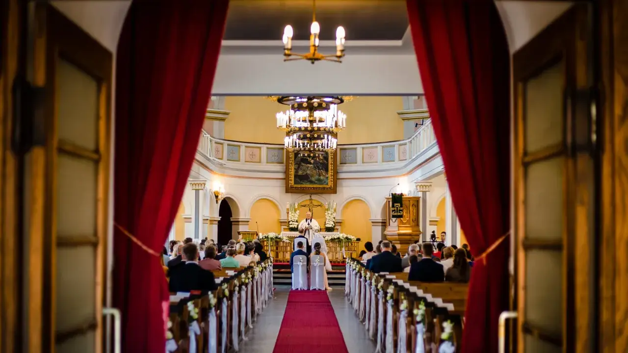W kościele trwa ślub jednostronny. Panna młoda i pan młody stoją przed ołtarzem, a ksiądz udziela im błogosławieństwa.