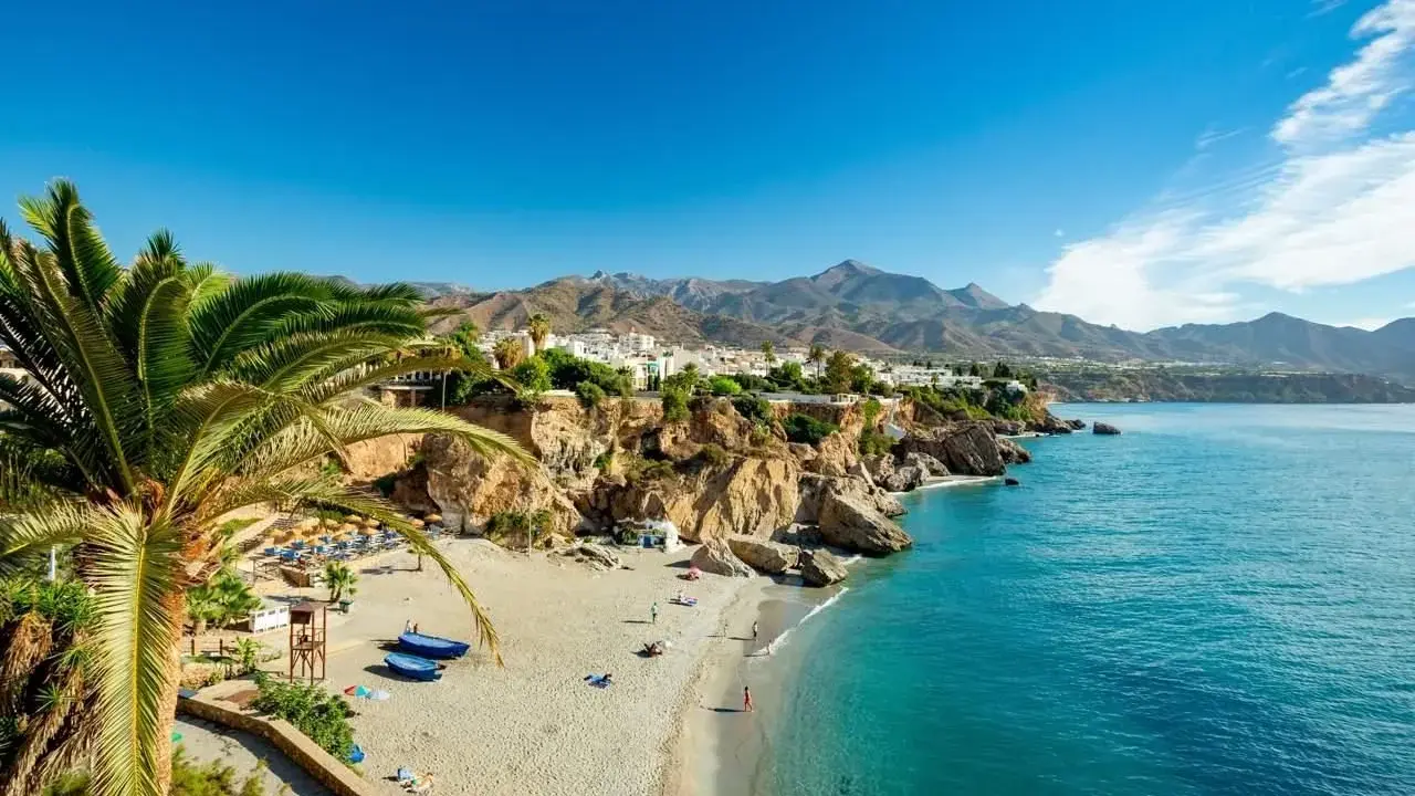 Sonnige playa de calahonda mit Palmen, weißem Sand, türkisfarbenem Meer und Bergen im Hintergrund.