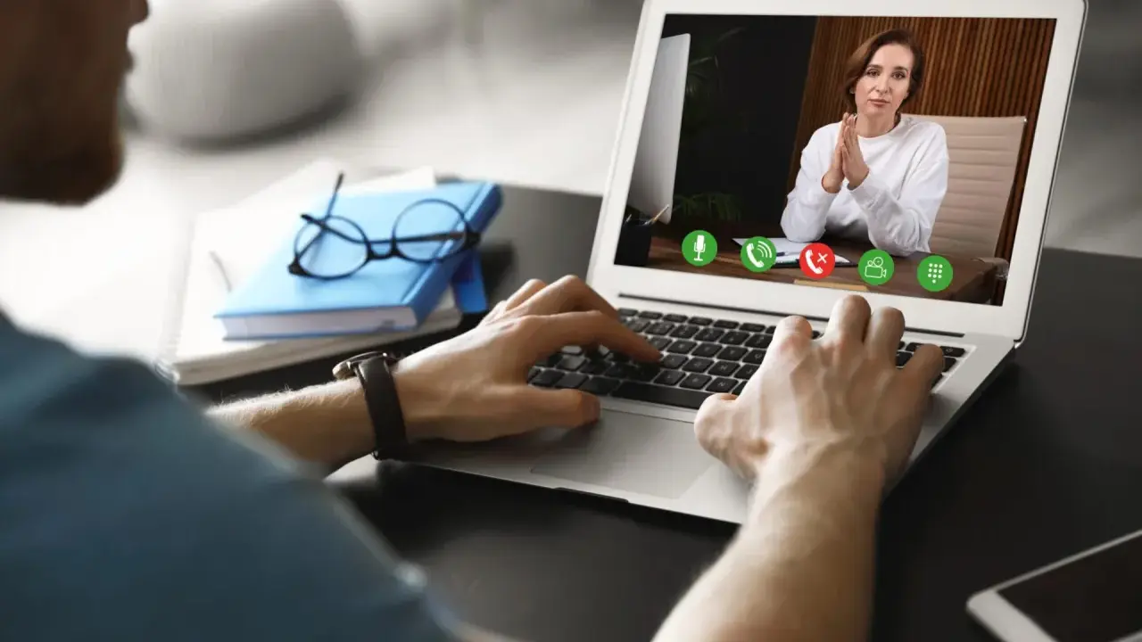 Mężczyzna prowadzi wirtualną superwizję przez laptopa. Na ekranie widać kobietę z dłońmi złożonymi w geście modlitwy.