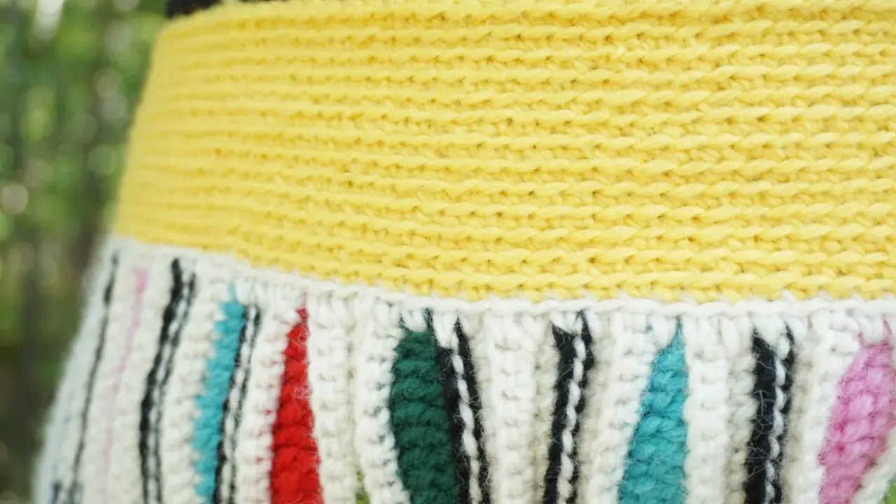 Detaljerad bild av en virkad kjol med gul resår och randigt mönster i vitt, rött, grönt, blått och rosa.