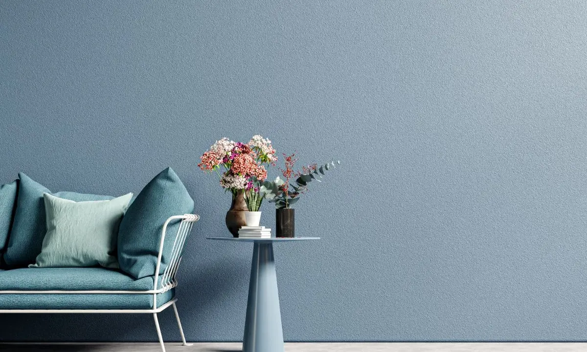 Divano blu petrolio e cuscini in tonalità pastello su sfondo azzurro polvere. Ottime idee colori pareti per un ambiente rilassante.