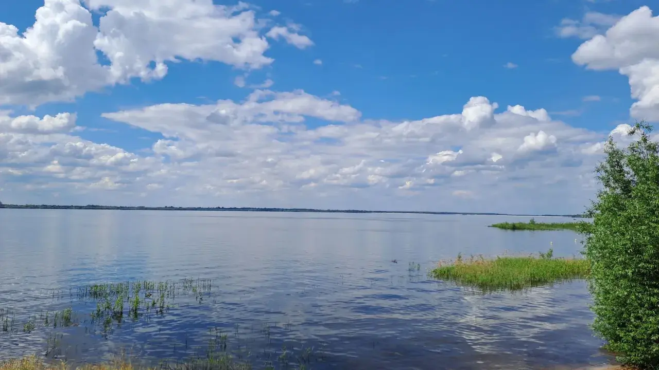 Spokojny zalew Jeziorsko w letni dzień. Błękitne niebo z białymi chmurami odbija się w tafli wody.