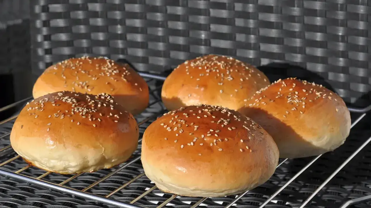 Fünf goldbraune Burgerbrötchen mit Sesam, perfekt für ein Burgerbrötchen-Rezept.