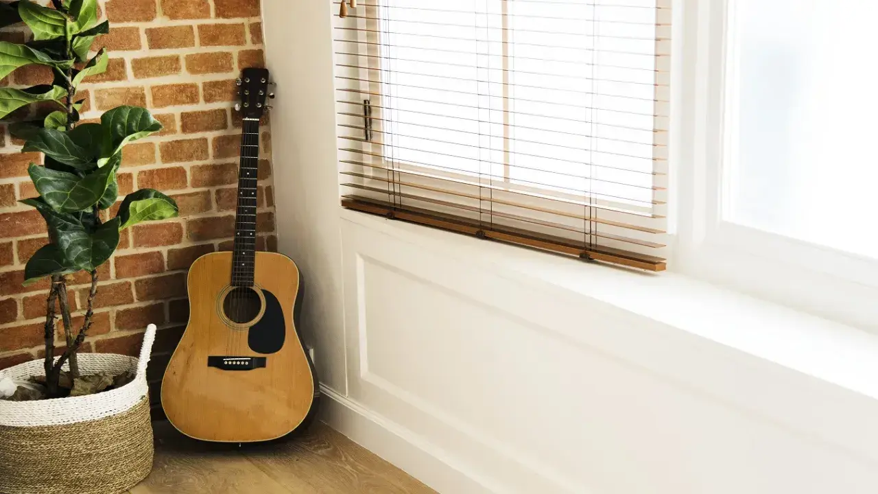 Gitara akustyczna obok ceglanej ściany i rośliny w koszu. Idealne miejsce na naukę piosenki na gitarę dla początkujących dzieci.
