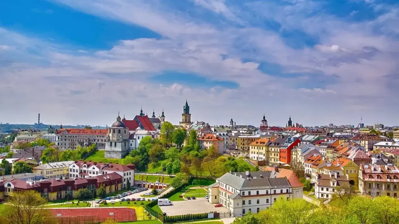Widok na malownicze miasto w województwie lubelskim. Dachy kamienic, kościoły i zieleń pod błękitnym niebem.
