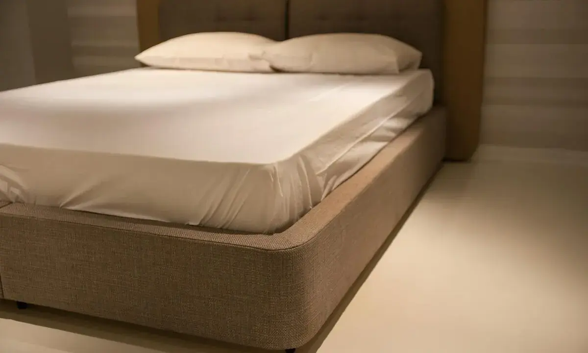 Un lit moderne avec un sommier tapissier, une base recouverte de tissu beige, prêt à accueillir un matelas blanc et des oreillers.