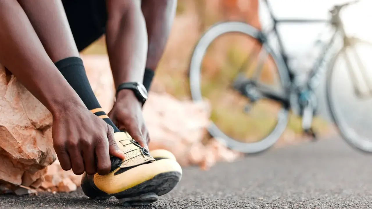 Rowerzysta zapina żółte buty, gotowy na kolejne wyzwania w **sporty rowerowe**. W tle widać rower.