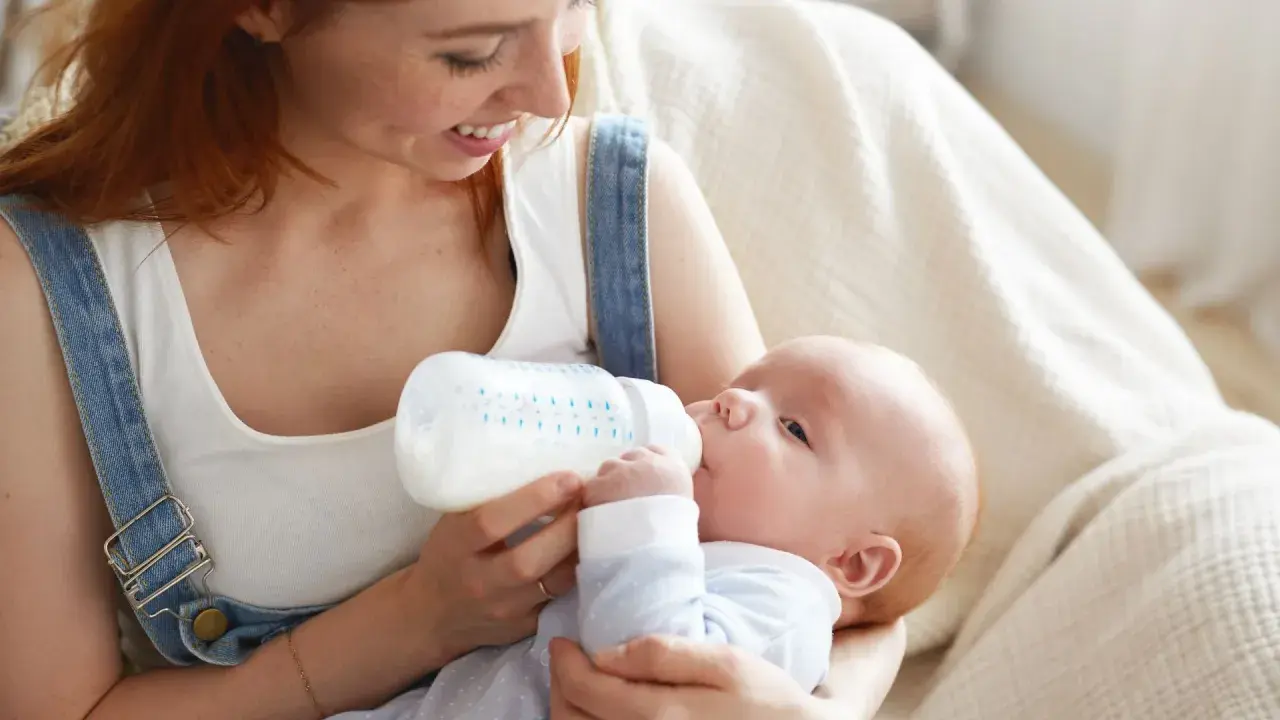Mamma con capelli rossi nutre il suo neonato con latte artificiale ogni 2 ore. Il piccolo beve con gusto dalla bottiglia.