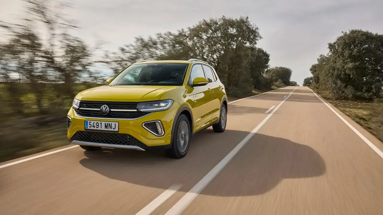 Un coche amarillo Volkswagen T-Cross circula por una carretera rural. ¿Cuánto se tarda en fabricar un coche? ¡Este parece listo para la carretera!