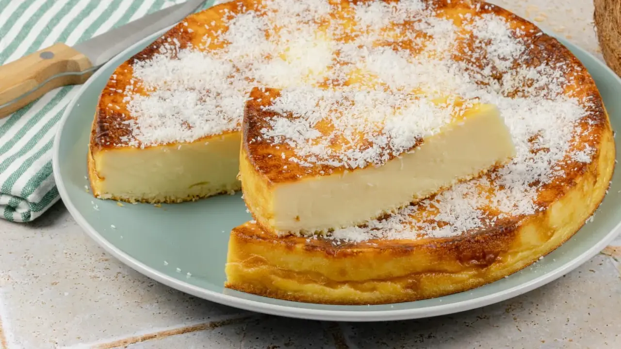 Un délicieux flan coco, saupoudré de noix de coco râpée, est servi sur une assiette. Une part est coupée et posée sur le dessus.