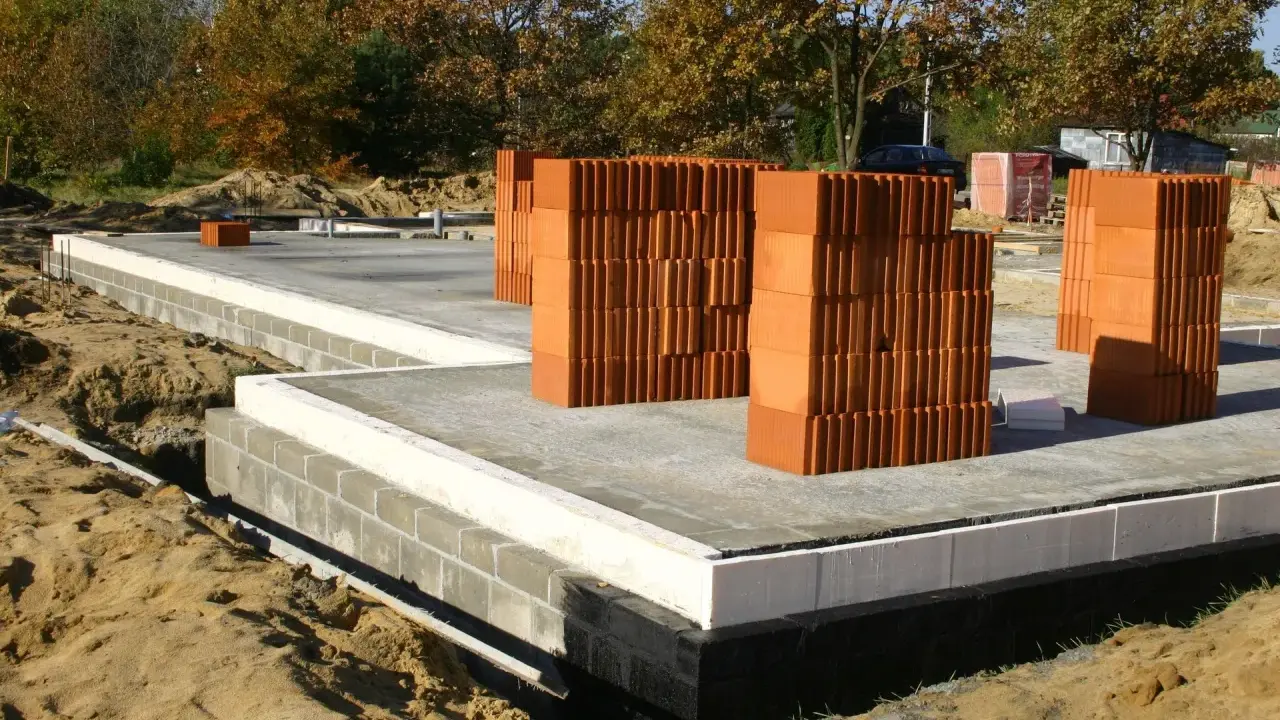Budowa domu w toku. Stosy cegieł, prawdopodobnie chudziak b10 czy b15, czekają na użycie. Fundamenty gotowe.