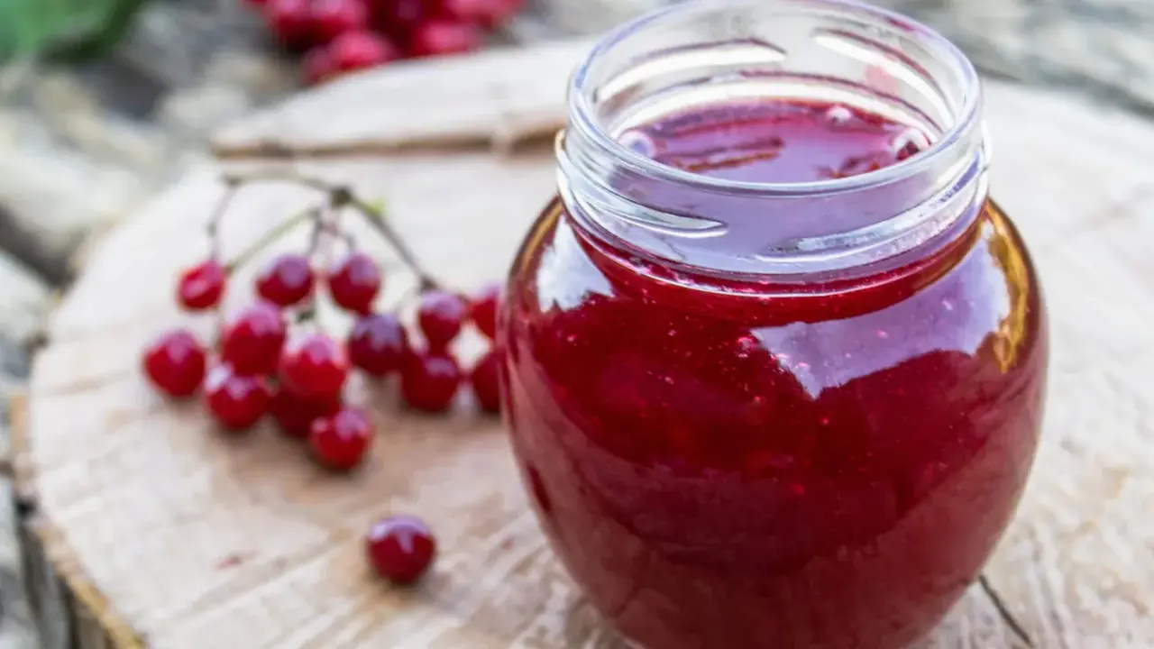 Un pot de gelee de groseille, aux reflets rubis, est posé sur une planche de bois. Des grappes de groseilles rouges sont disposées à côté.