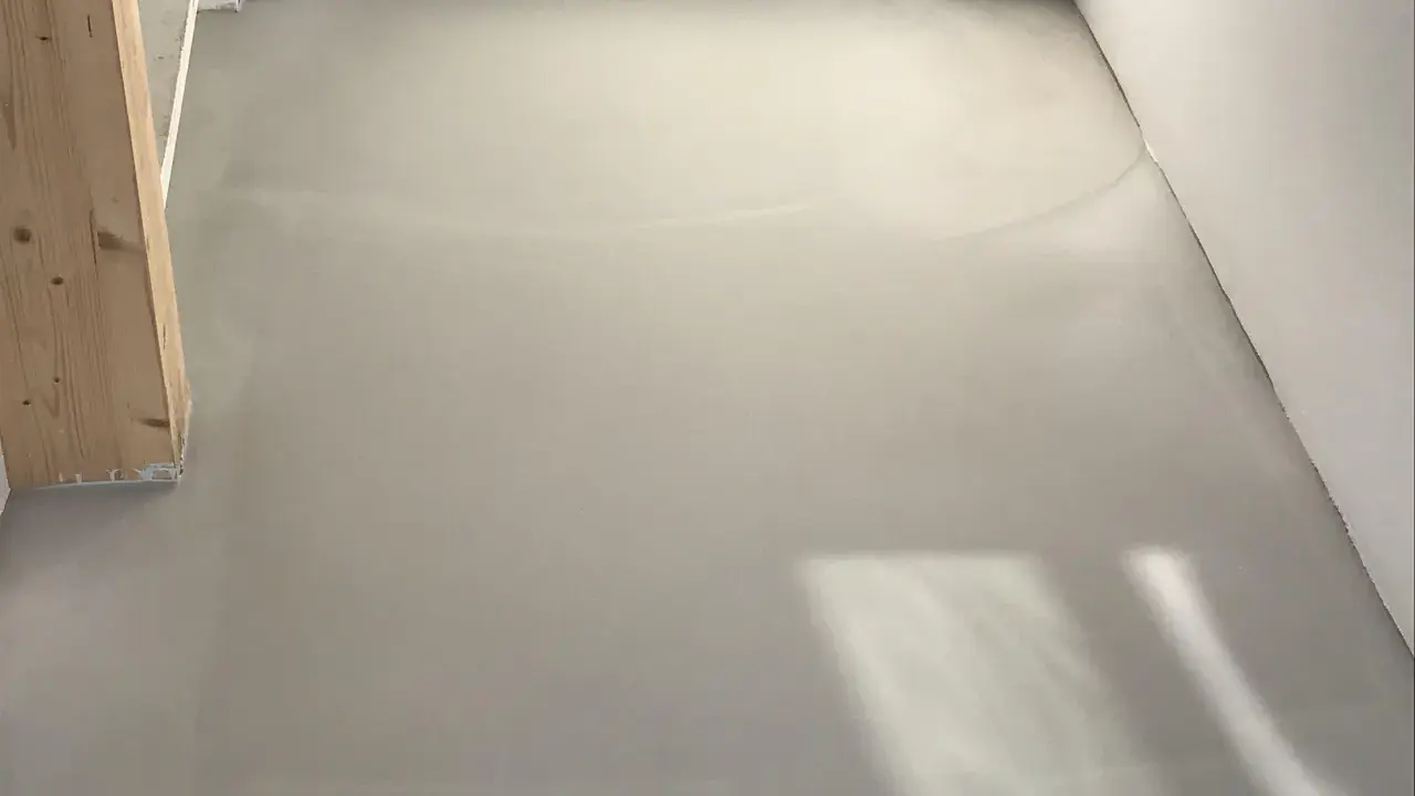 Pavimento in resina grigia, simile a un massetto, con un pilastro di legno. Potrebbe essere un'idea per pavimenti in pvc svantaggi, ma questa è una finitura grezza.