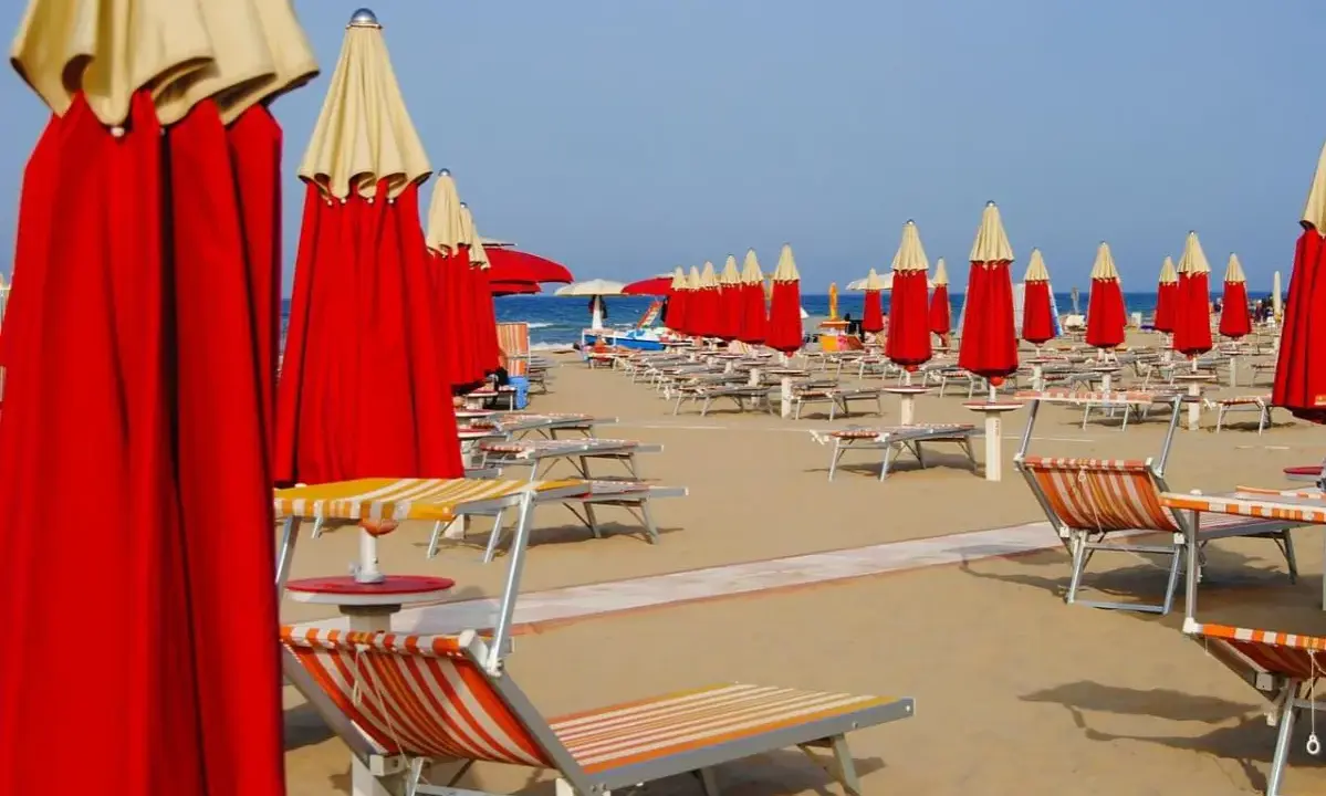 Filettate di lettini e ombrelloni rossi e gialli sulla spiaggia di Rimini Nord, pronti per accogliere i bagnanti.