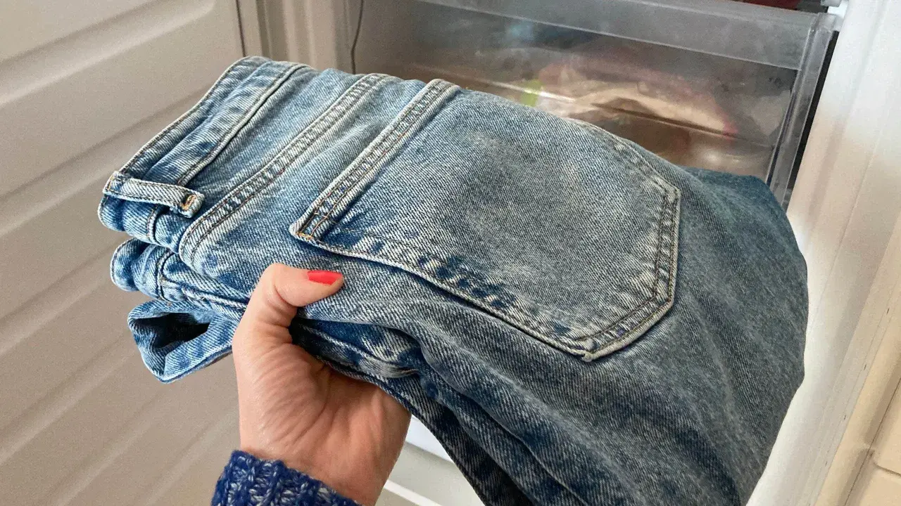 Hand håller nya jeans som luktar illa, placerade i en frys för att fräscha upp dem.