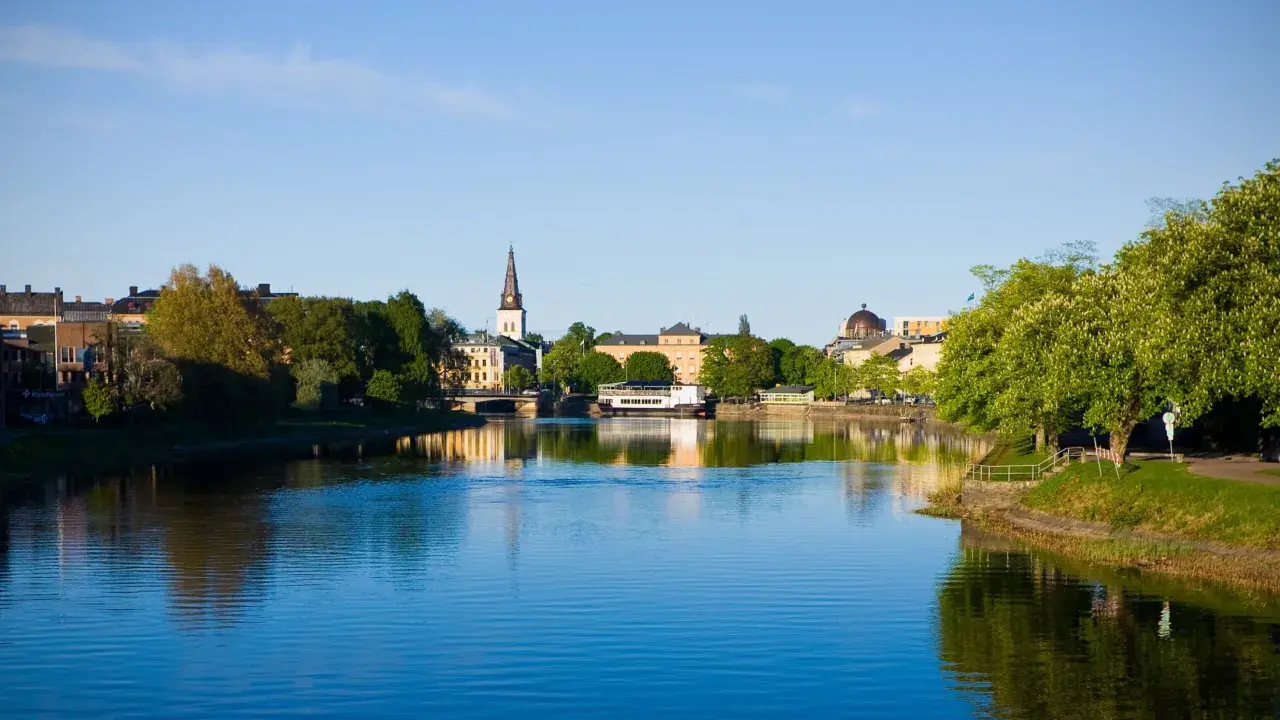 Vacker vy över Klarälven i Karlstad med stadens silhuett och grönska. Perfekt för promenader och andra aktiviteter Karlstad erbjuder.