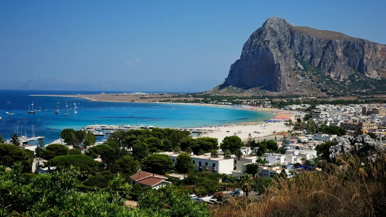 Vista panoramica di San Vito Lo Capo, con la spiaggia affollata e il Monte Monaco. La distanza da Cefalù è di circa 100 km.