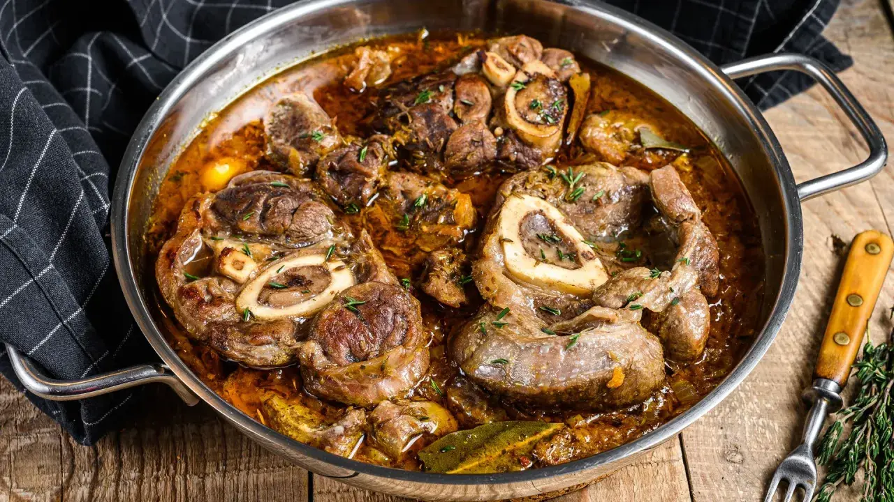 Ossobuco que es: jugosas rodajas de ternera cocinadas a fuego lento en una rica salsa con hierbas y especias, servidas en una sartén metálica.