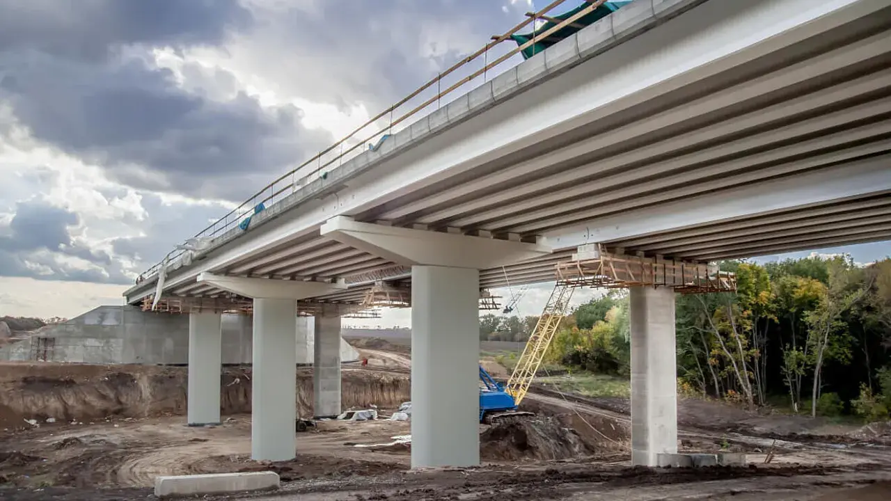Construcción de un puente de viga con pilares de hormigón y grúa amarilla en el sitio.