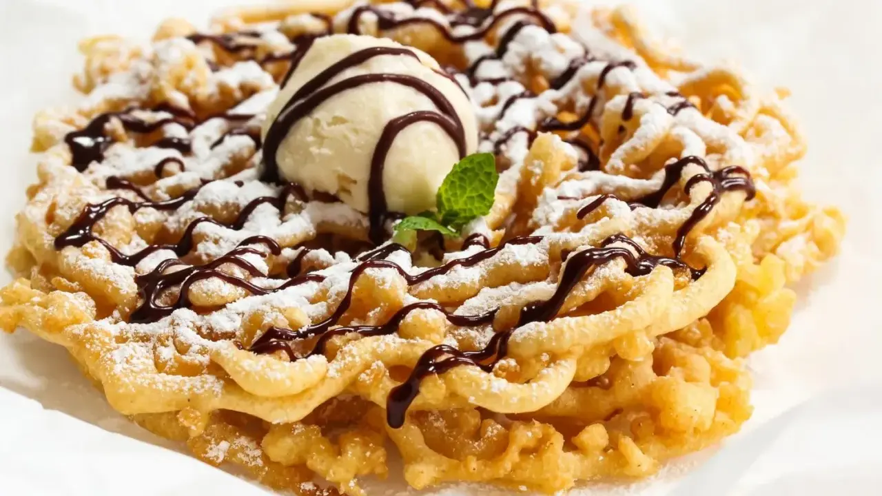 Pyszny funnel cake posypany cukrem pudrem, polany czekoladą i udekorowany gałką lodów waniliowych.