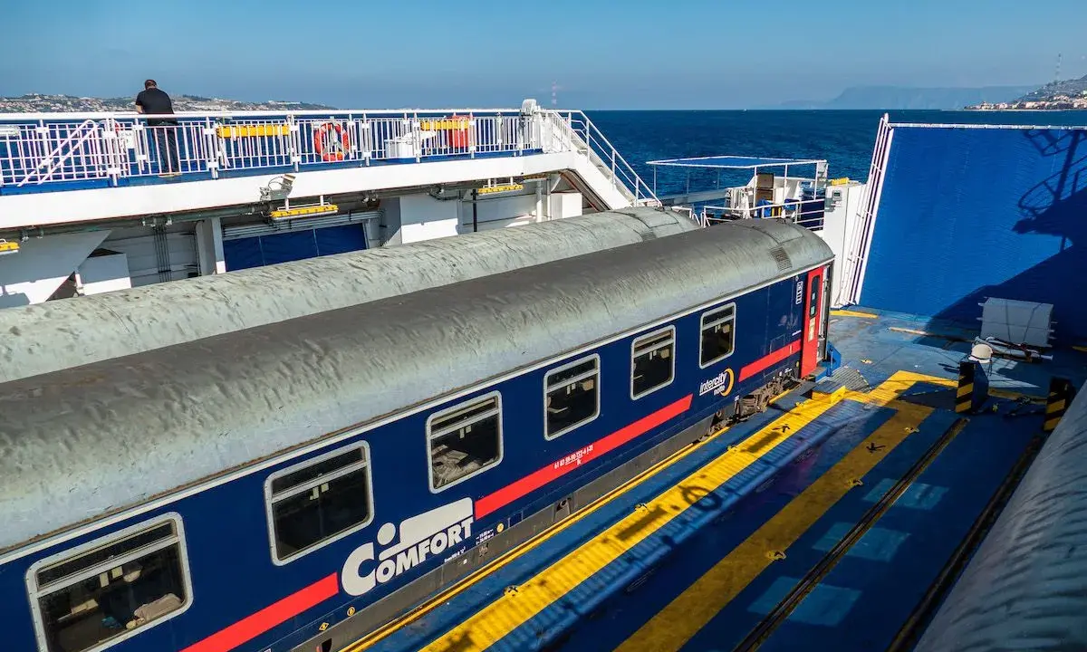 Ein blauer Nachtzug nach Palermo steht auf einer Fähre. Ein Mann blickt aufs Meer.