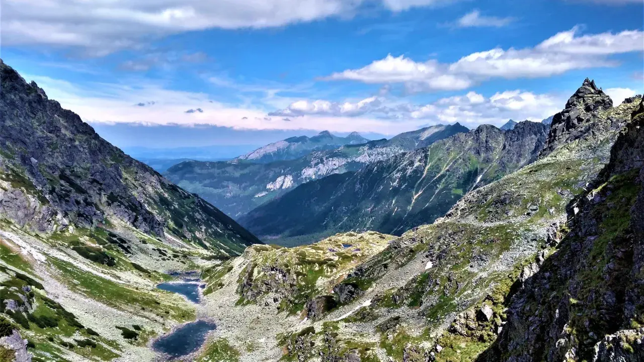 Majestatyczne Tatry Wysokie z doliną, dwoma stawami i skalistymi szczytami pod błękitnym niebem.