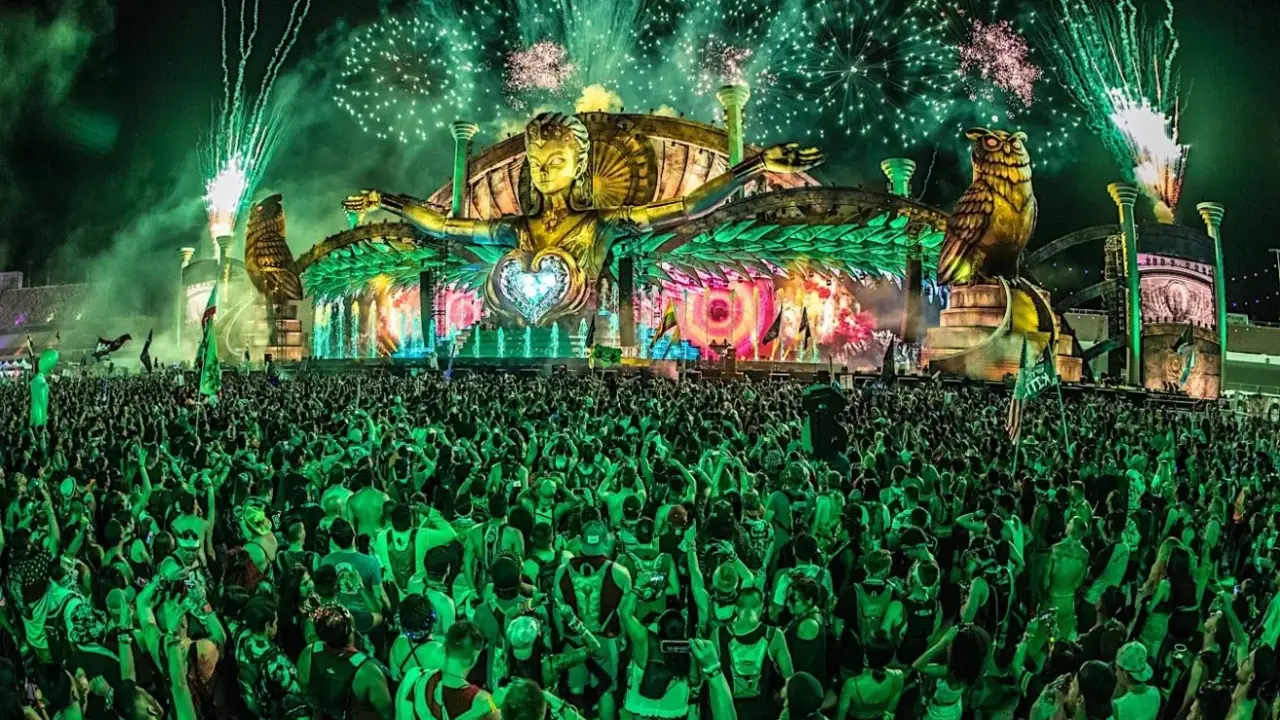 Folla immensa sotto un palco spettacolare con fuochi d'artificio verdi, uno dei rave party più famosi al mondo.