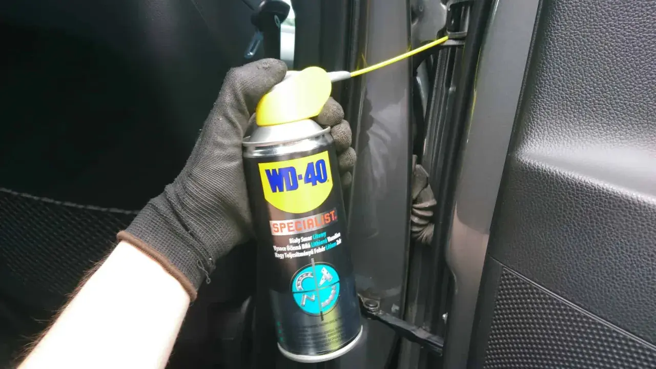 Ręka w rękawiczce aplikuje smar do zawiasów drzwi samochodowych WD-40 Specialist.