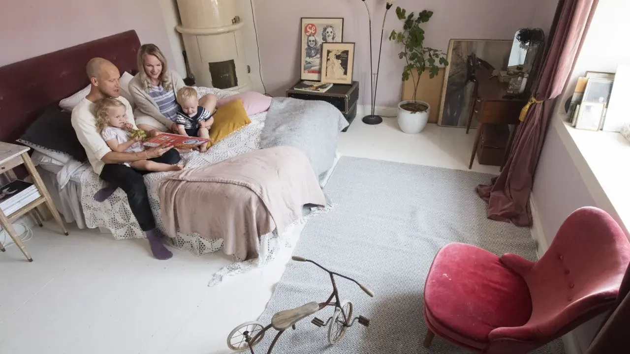 Familjen myser i sängen, pappan läser en bok för barnen. Ett litet bo med barn som njuter av stunden.
