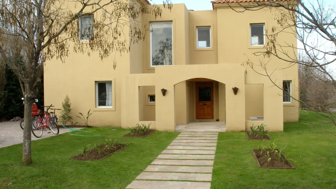Una encantadora casa color arena con techo de tejas rojas, un camino de losas y dos bicicletas aparcadas en el jardín.