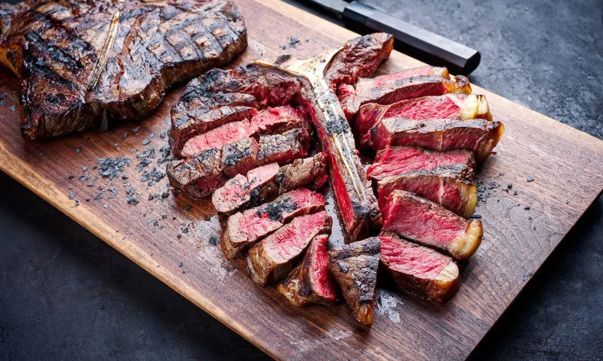 Una succulenta fiorentina alla griglia, affettata e servita su un tagliere di legno, con sale grosso sparso.