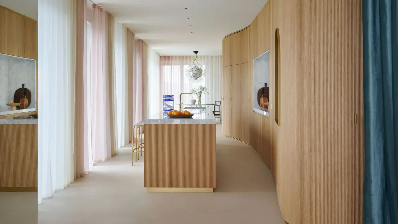 Interno moderno con isola cucina in legno e boiserie curvilinea. Tende leggere color pastello creano un'atmosfera soffusa.