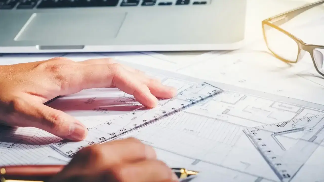 Rysowanie planów, laptop i okulary na biurku. Zastanawiasz się, ile zarabia architekt?