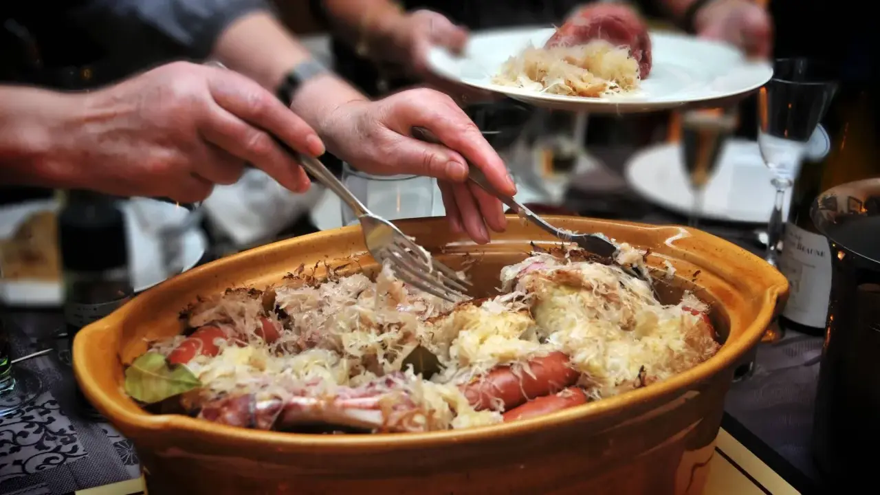 Un plat généreux de choucroute garnie, spécialité de la gastronomie alsacienne, est servi. Des mains servent ce délice, promesse d'une savoureuse nourriture d'Alsace.