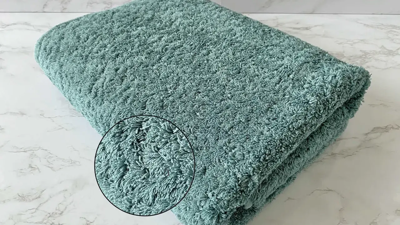 A folded teal terry cloth towel with a magnified inset showing its plush texture.