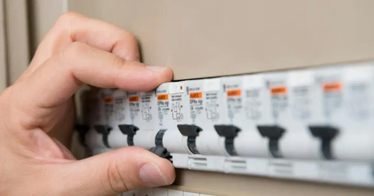 Main d'une personne actionnant un disjoncteur dans un tableau électrique. Les plombs ont sauté, il faut rétablir le courant.