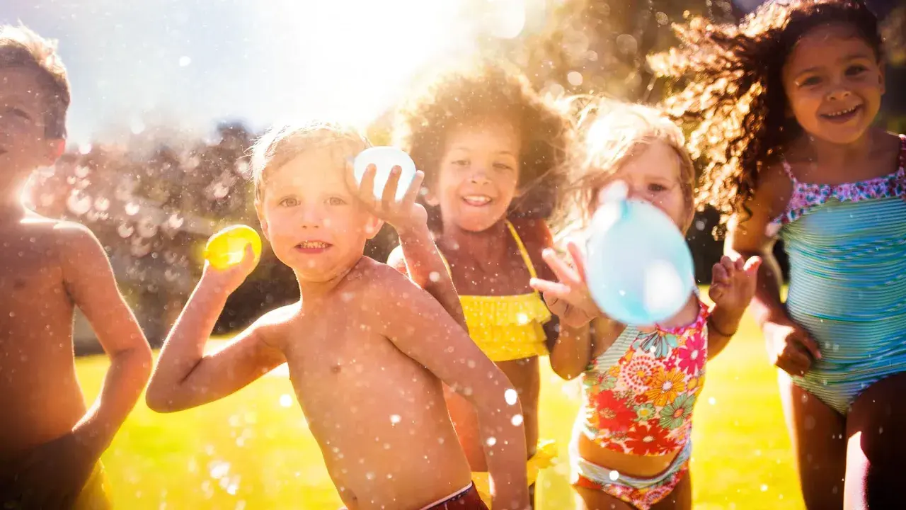 Niños riendo y jugando con globos de agua bajo el sol. Salpicaduras y diversión garantizada en estos juegos acuáticos.