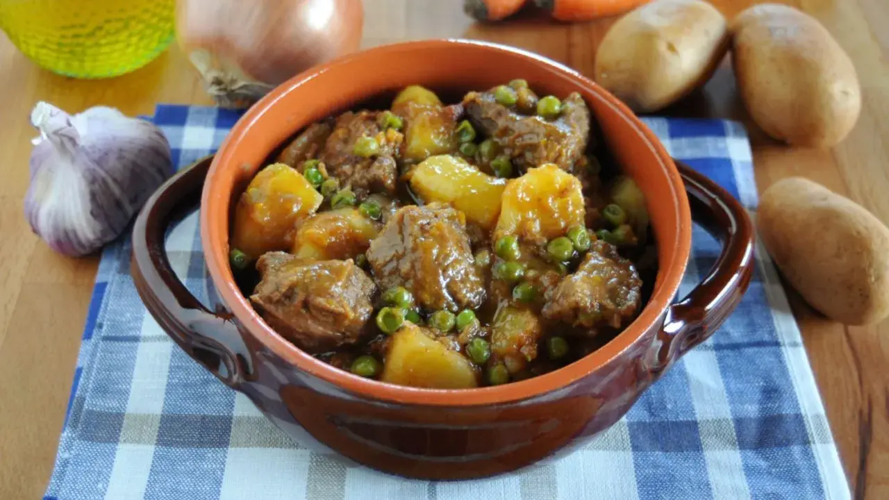 Un saporito spezzatino con patate e piselli, servito in una ciotola di terracotta, con ingredienti freschi sullo sfondo.